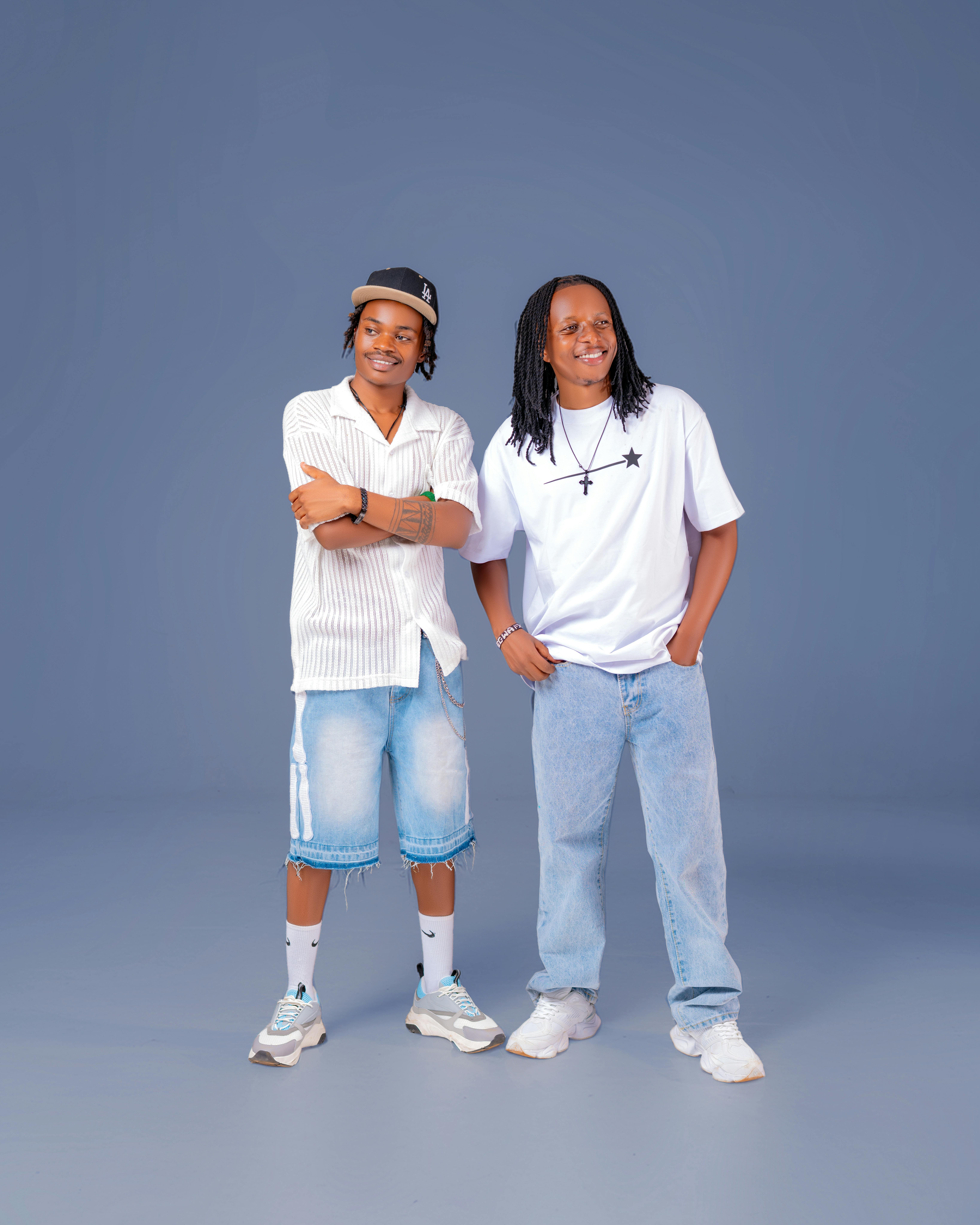 Two young adults wearing casual denim and white outfits, posing confidently on a blue background.