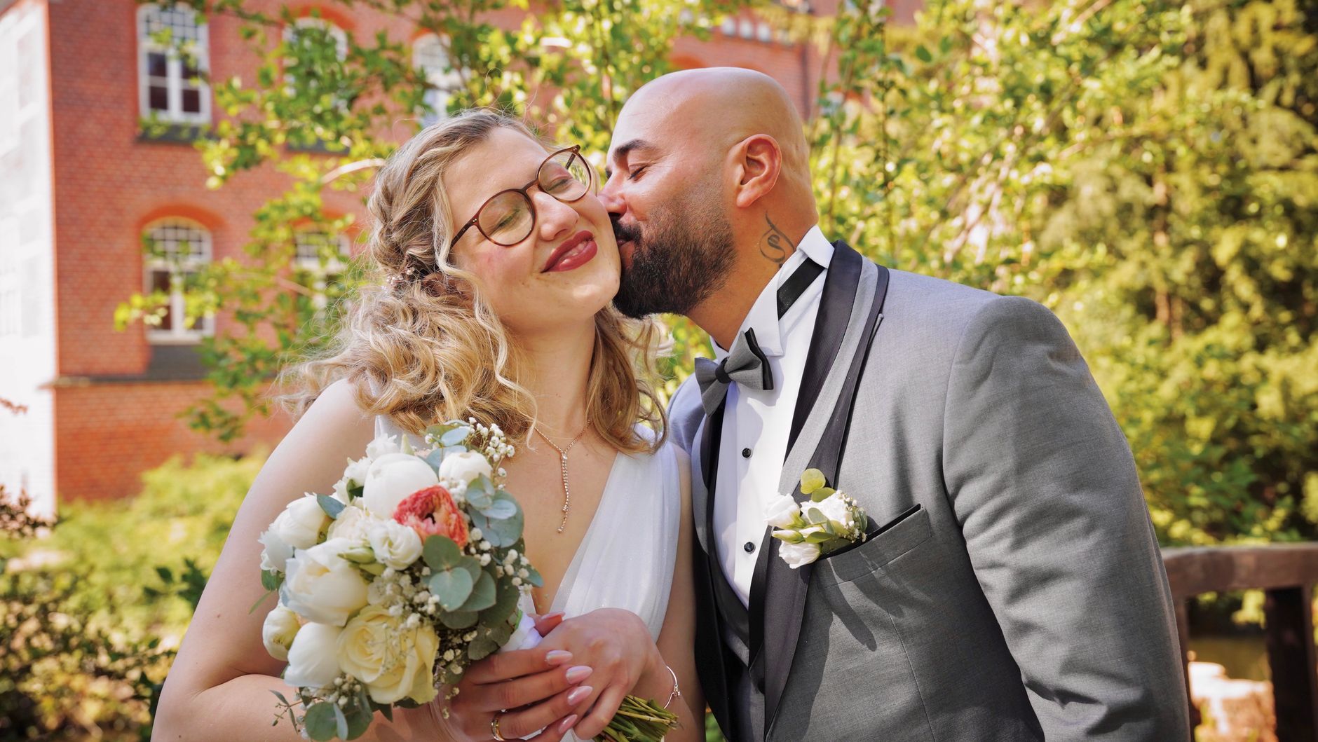 A joyful wedding couple shares a tender kiss outdoors in Hamburg, showcasing love and celebration.