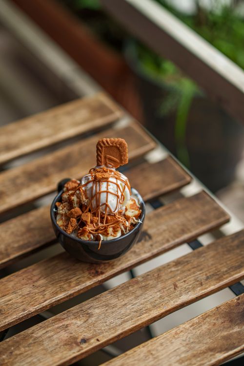 Free Tempting ice cream with caramel drizzle and cookie topping on a wooden table outdoors. Stock Photo
