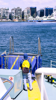 Individual on ferry with city skyline and water view in background.