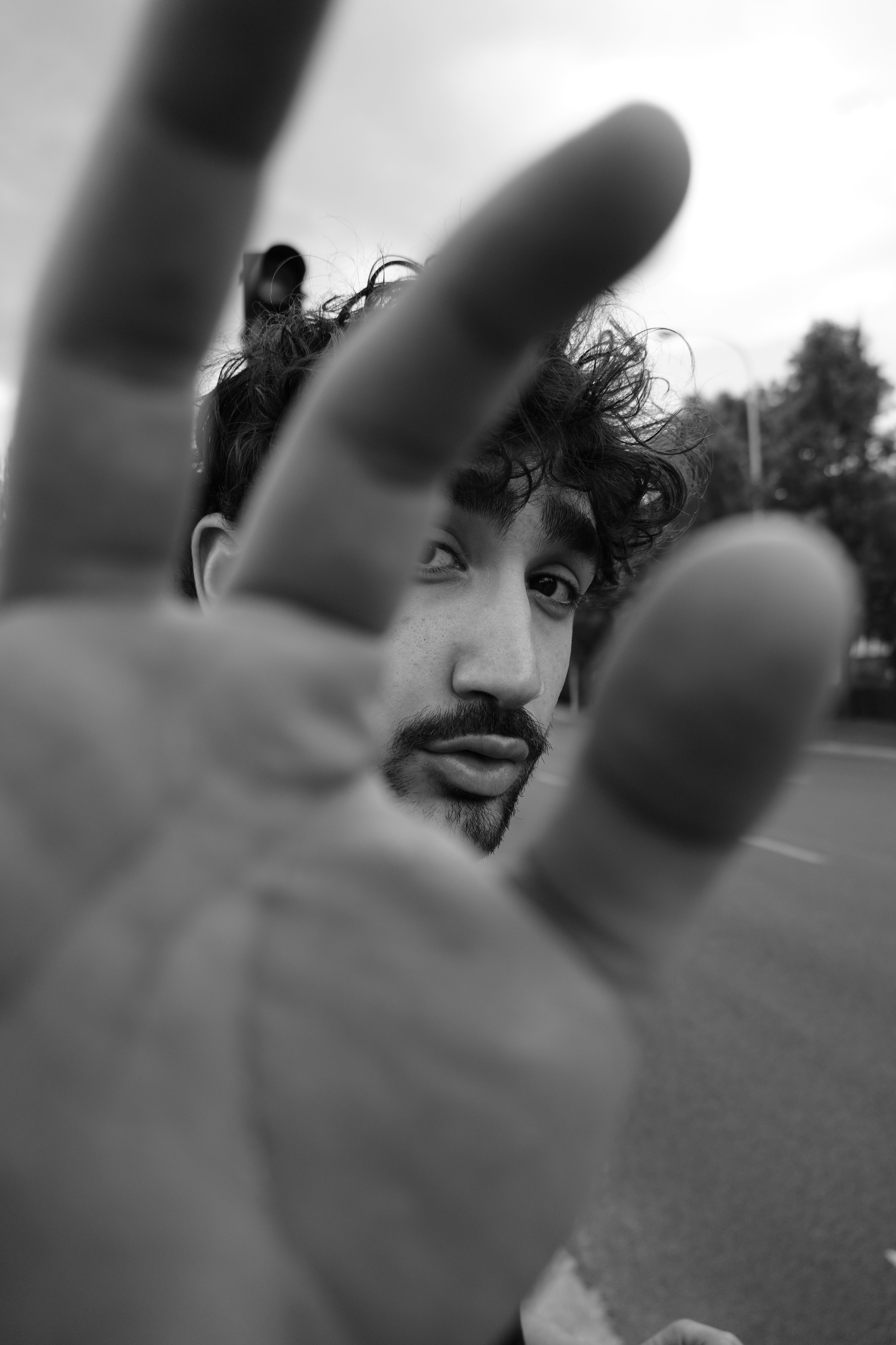Artistic black and white portrait of a man with a hand gesture obscuring part of his face.