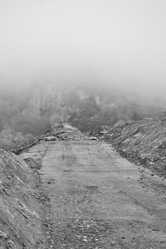 A deserted road leads through fog-covered mountains, creating a mysterious, moody scene.