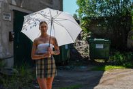 Young woman in fashion outfit stands with umbrella in urban Tallinn.