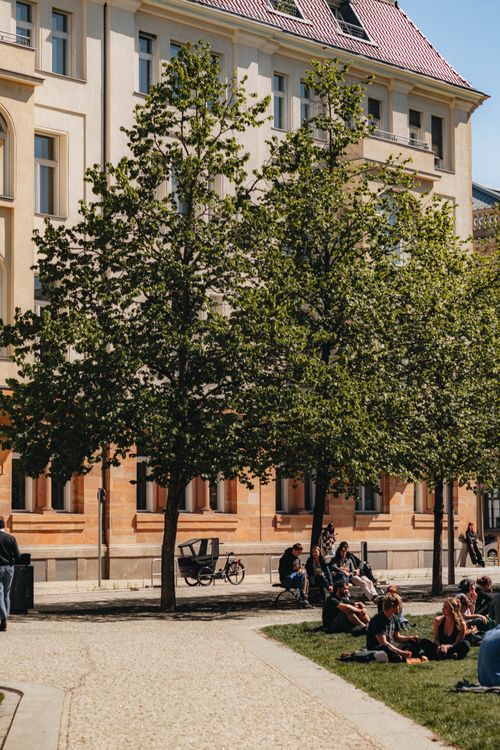 Free People enjoying a sunny day at a city square in Berlin with trees and a historic building. Stock Photo