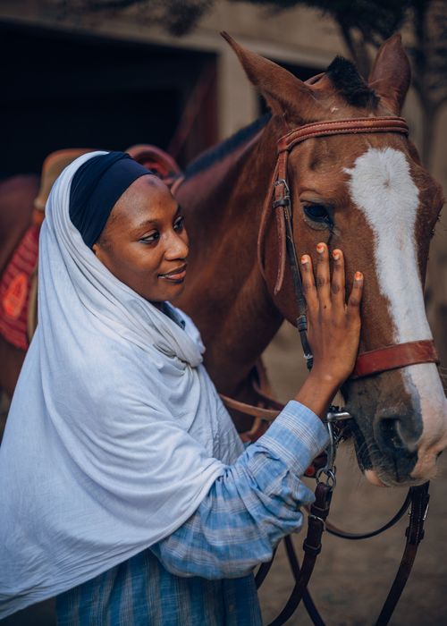 Free A Nigerian woman gently caressing a horse outdoors in cultural attire. Stock Photo