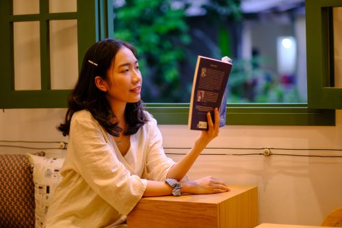 Free Serene scene of a young woman enjoying a book by a window in Hue, Vietnam. Stock Photo