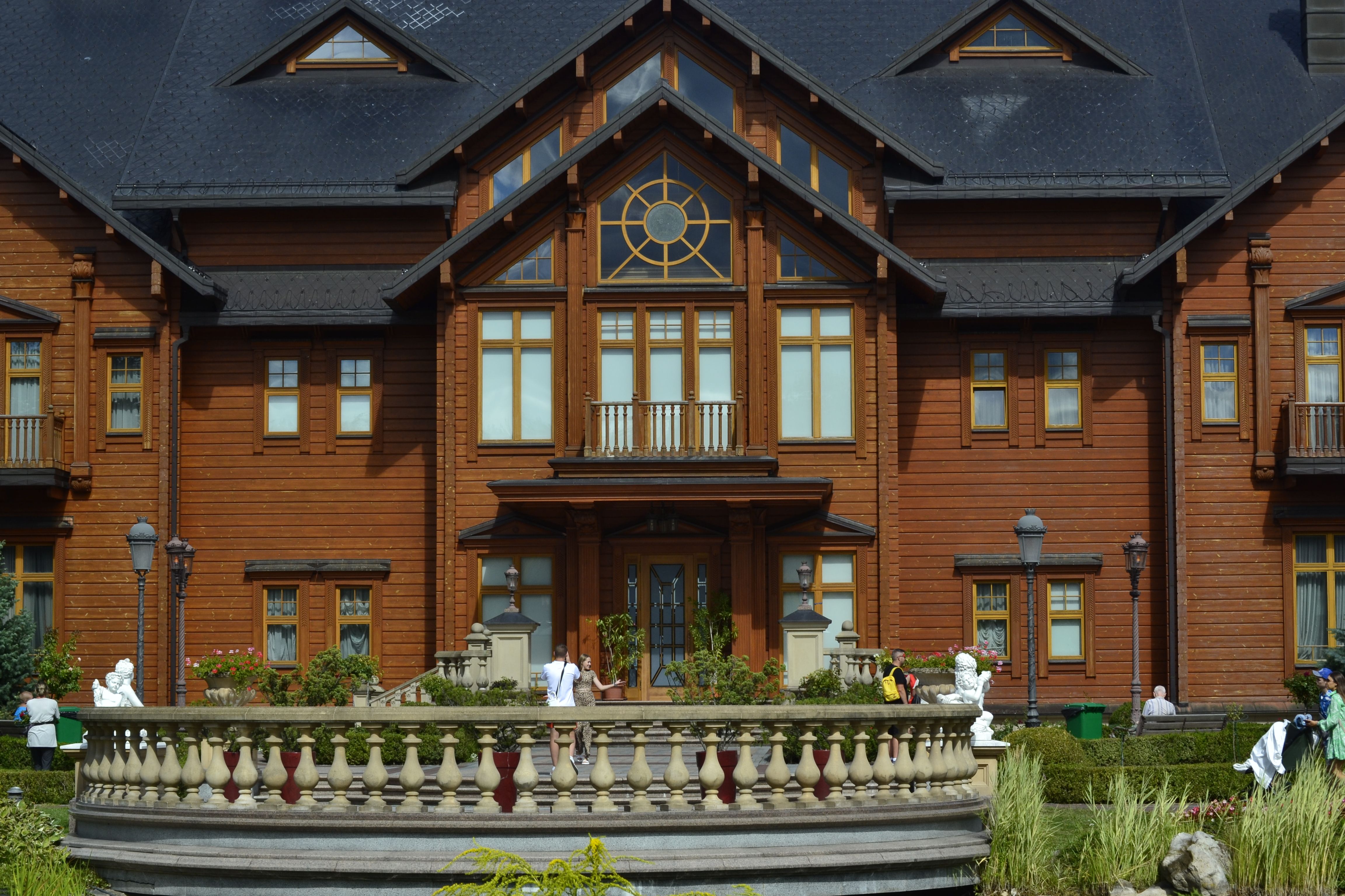 Front view of a large wooden mansion with intricate architectural details and a spacious outdoor terrace.