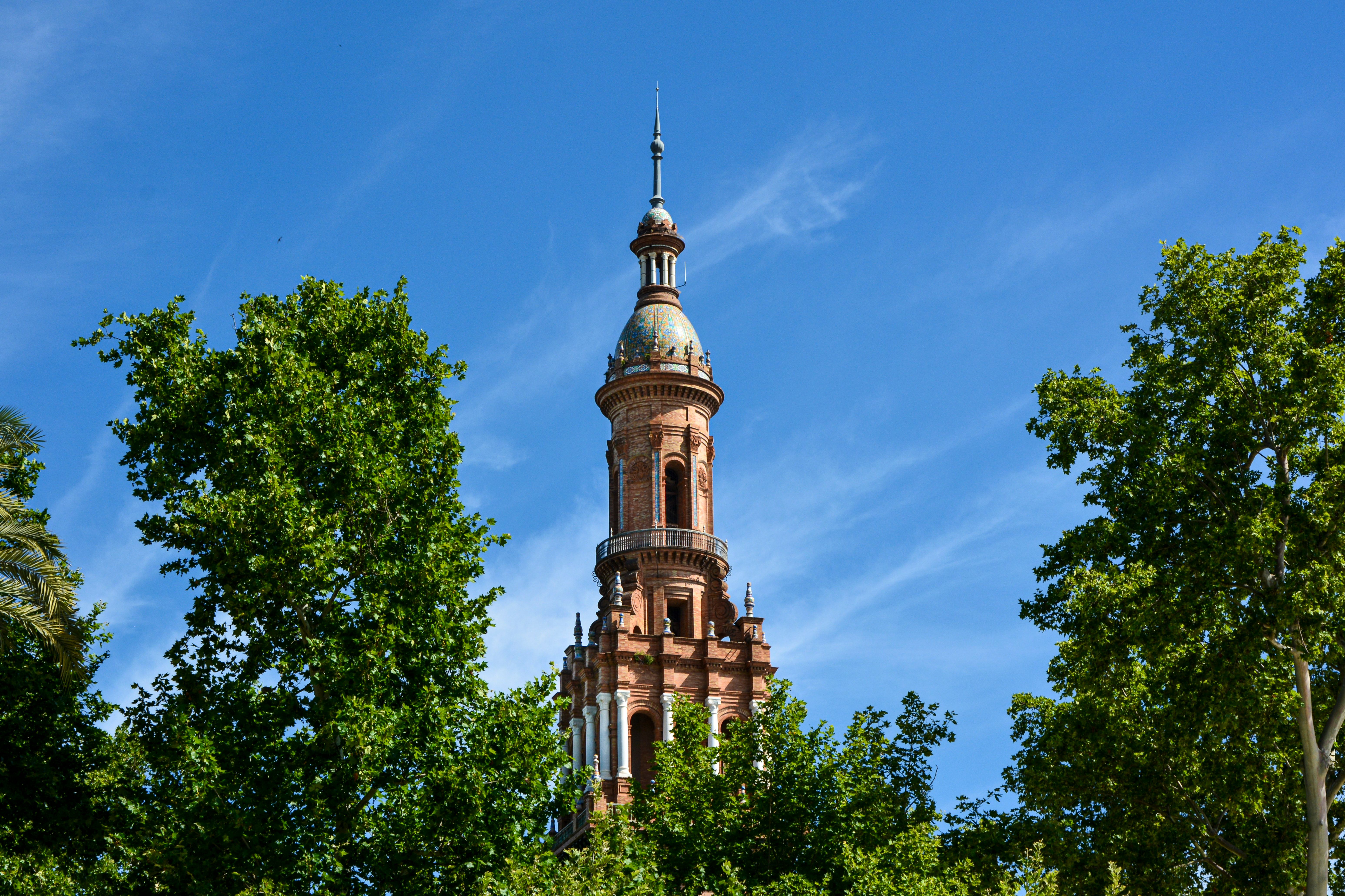 Beautiful historic tower rising above lush green trees in Sevilla, Spain.