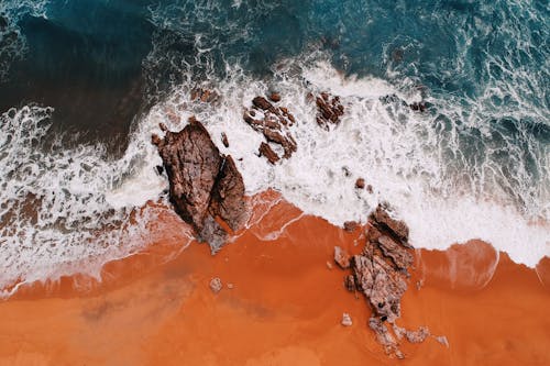 Drone view of foamy wave running on sandy shore with rocks and cliffs