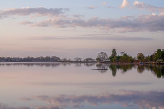 Peaceful lake scene at sunrise with calm waters and pastel skies reflecting a tranquil mood.