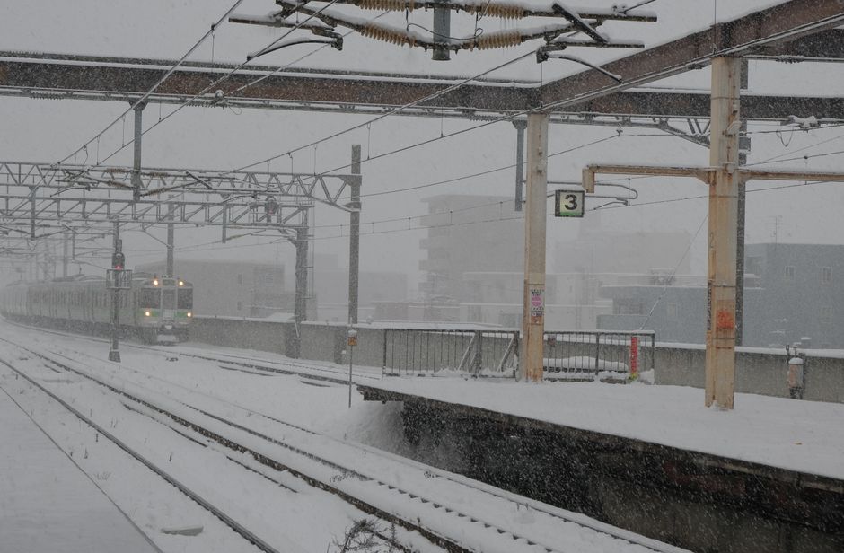 激しい降雪の中、雪に覆われた駅に近づく列車。冬の日の旅の風景。