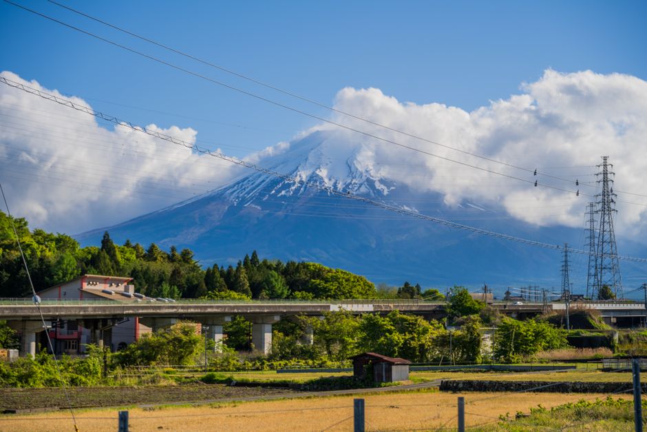 Scenic view of Mount Fuji with clouds, power lines, and vibrant greenery in the foreground.