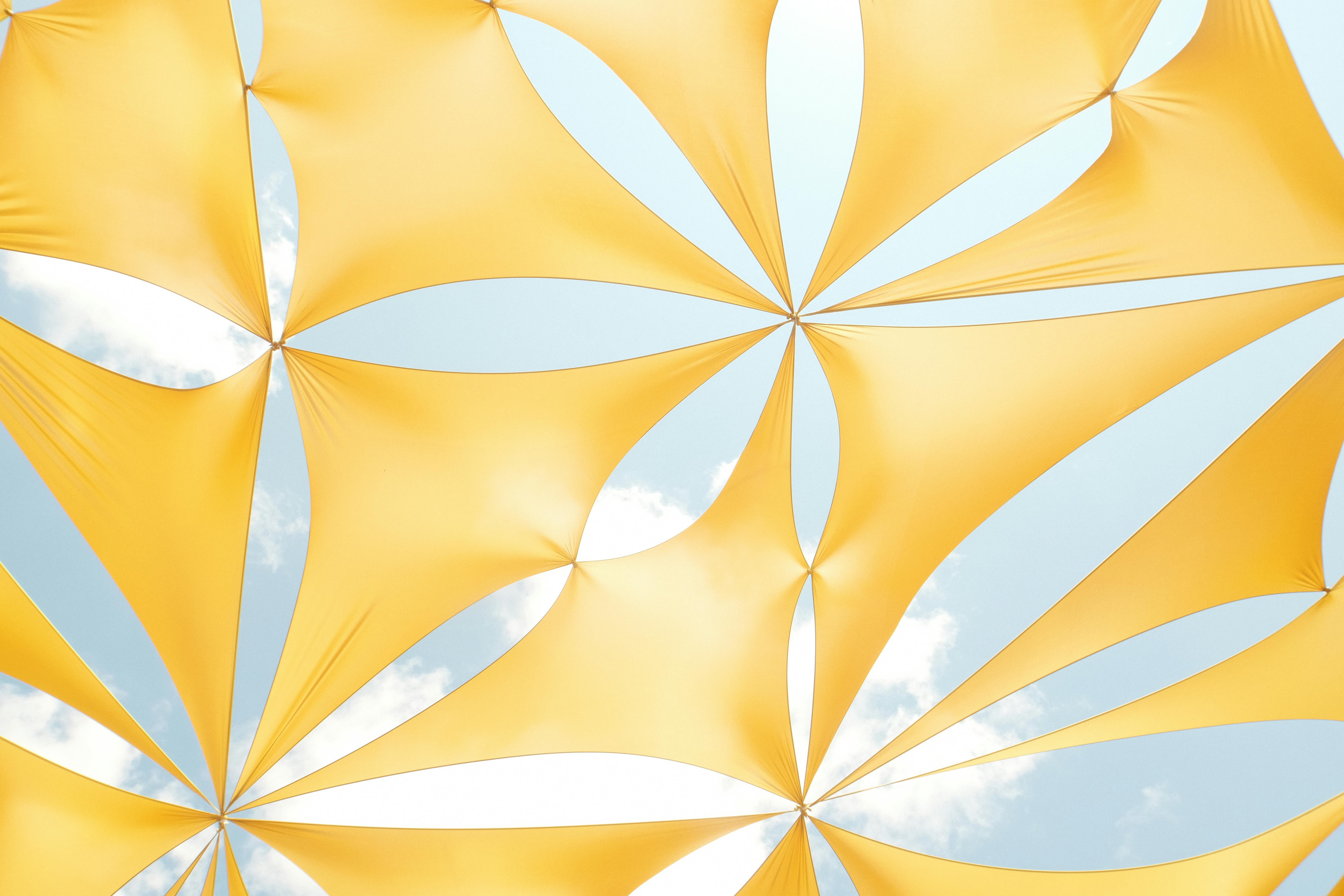 Bright yellow fabric canopy forming abstract patterns against a clear blue sky.