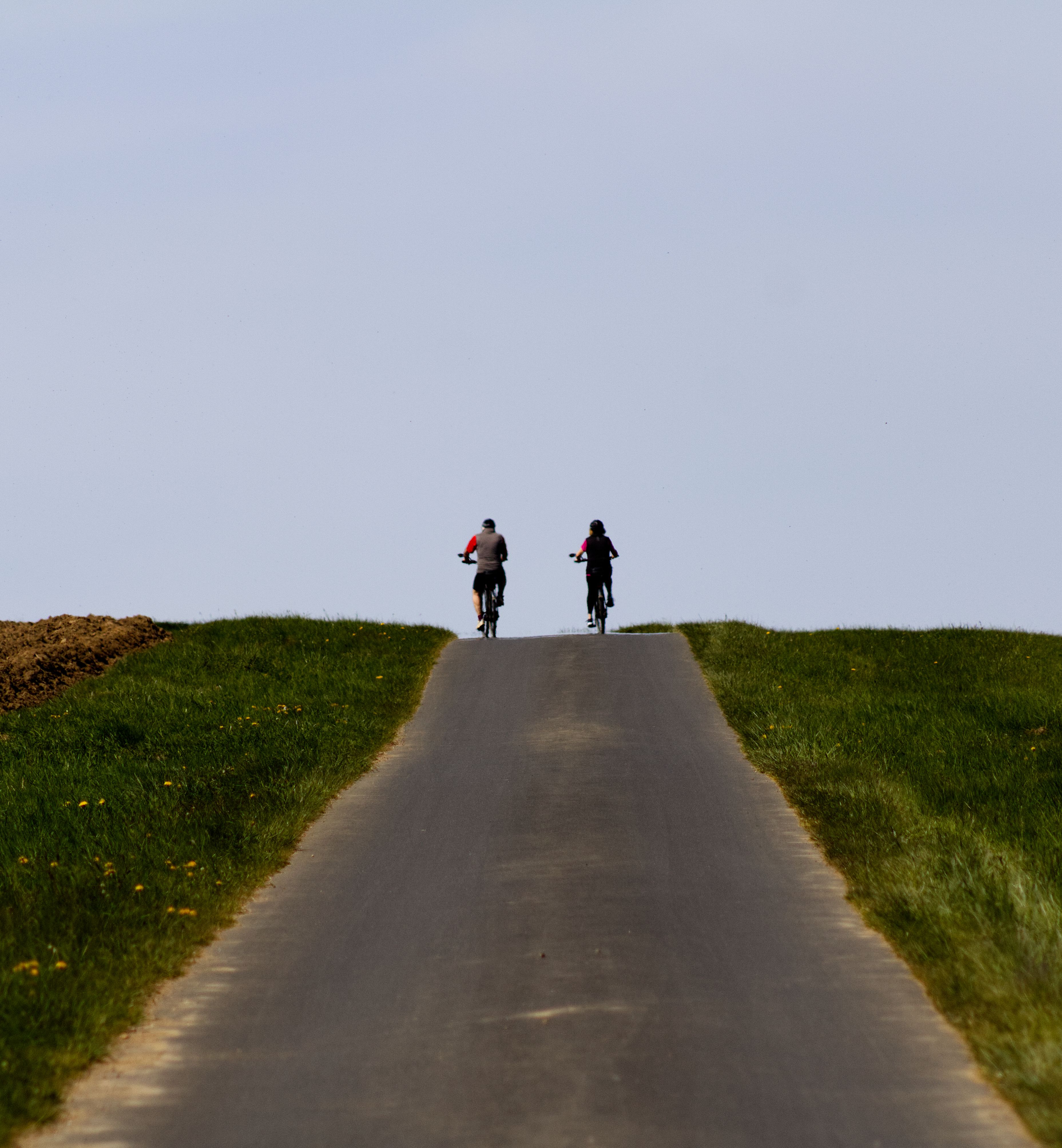 Two cyclists ascend a picturesque road surrounded by lush greenery under a clear sky in Germany.