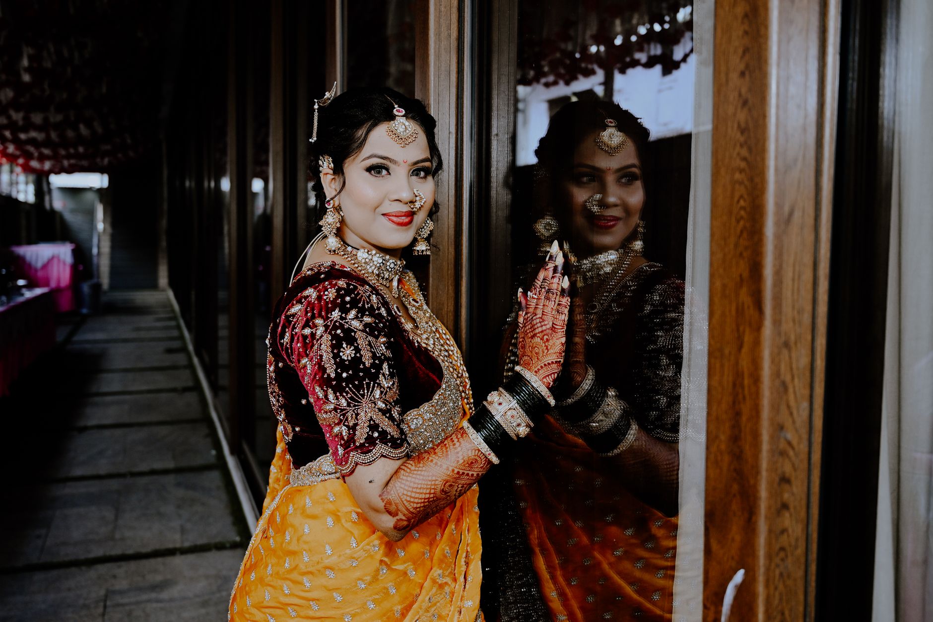 Stunning Indian bride in traditional outfit with intricate jewelry and henna, gazing at her reflection.