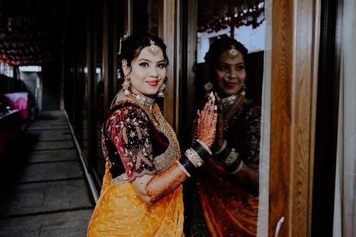 Free Stunning Indian bride in traditional outfit with intricate jewelry and henna, gazing at her reflection. Stock Photo