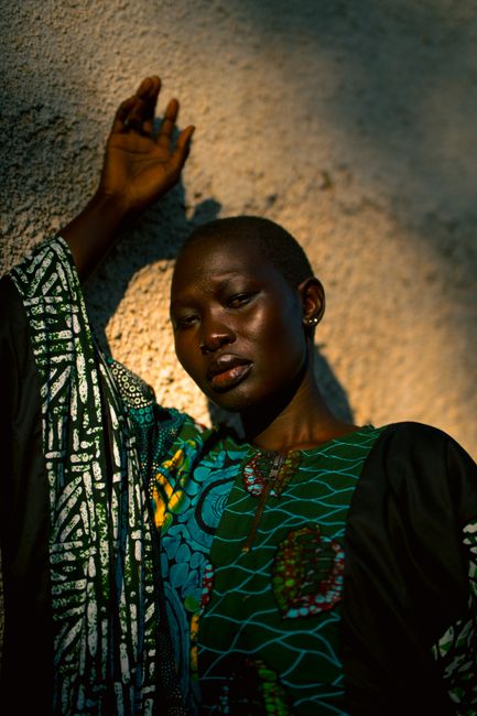 Artistic portrait of a woman in traditional African attire against a textured wall.