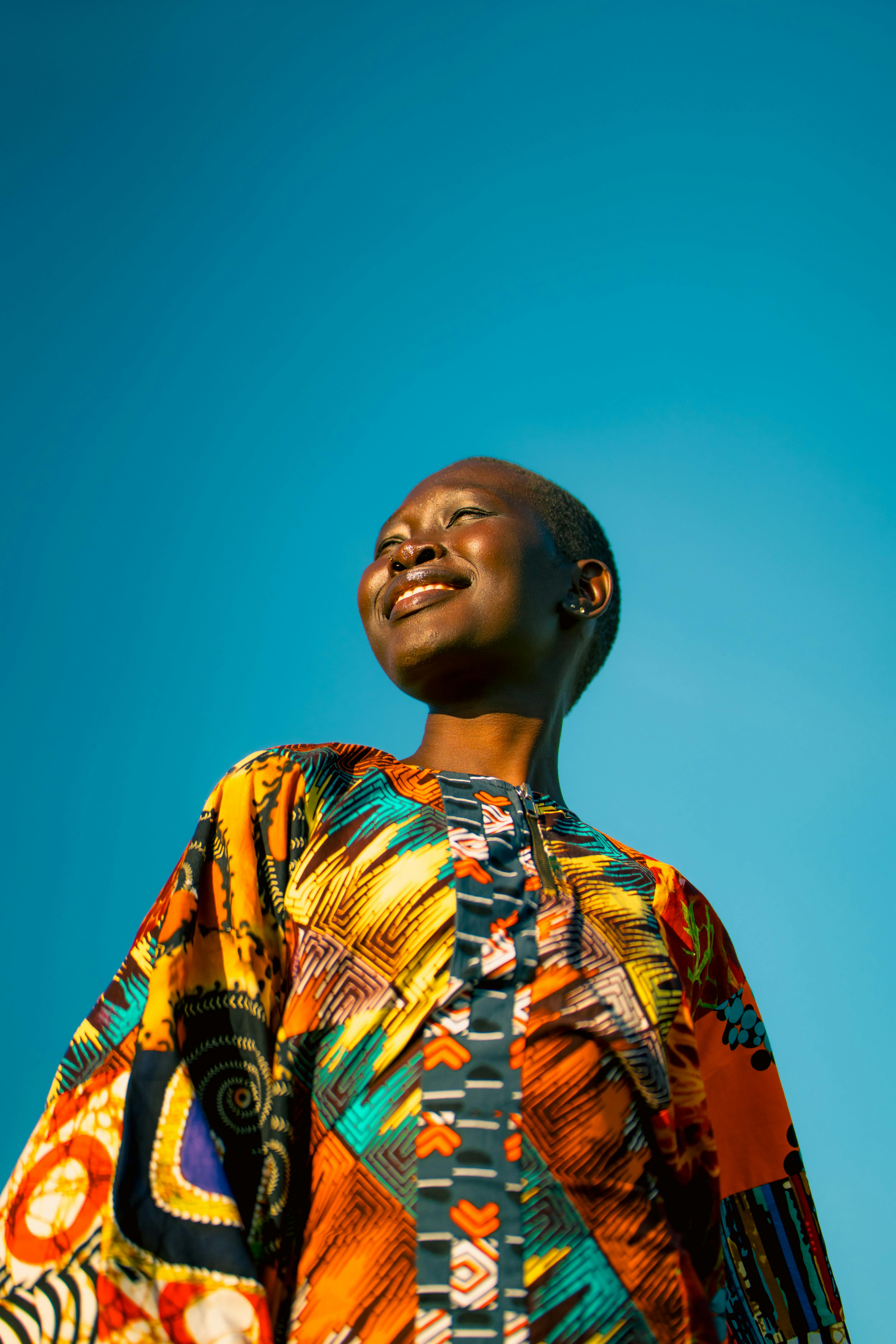 Vibrant portrait of a smiling woman in colorful attire against a clear blue sky.