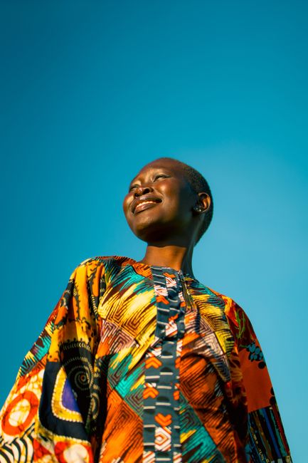 Vibrant portrait of a smiling woman in colorful attire against a clear blue sky.