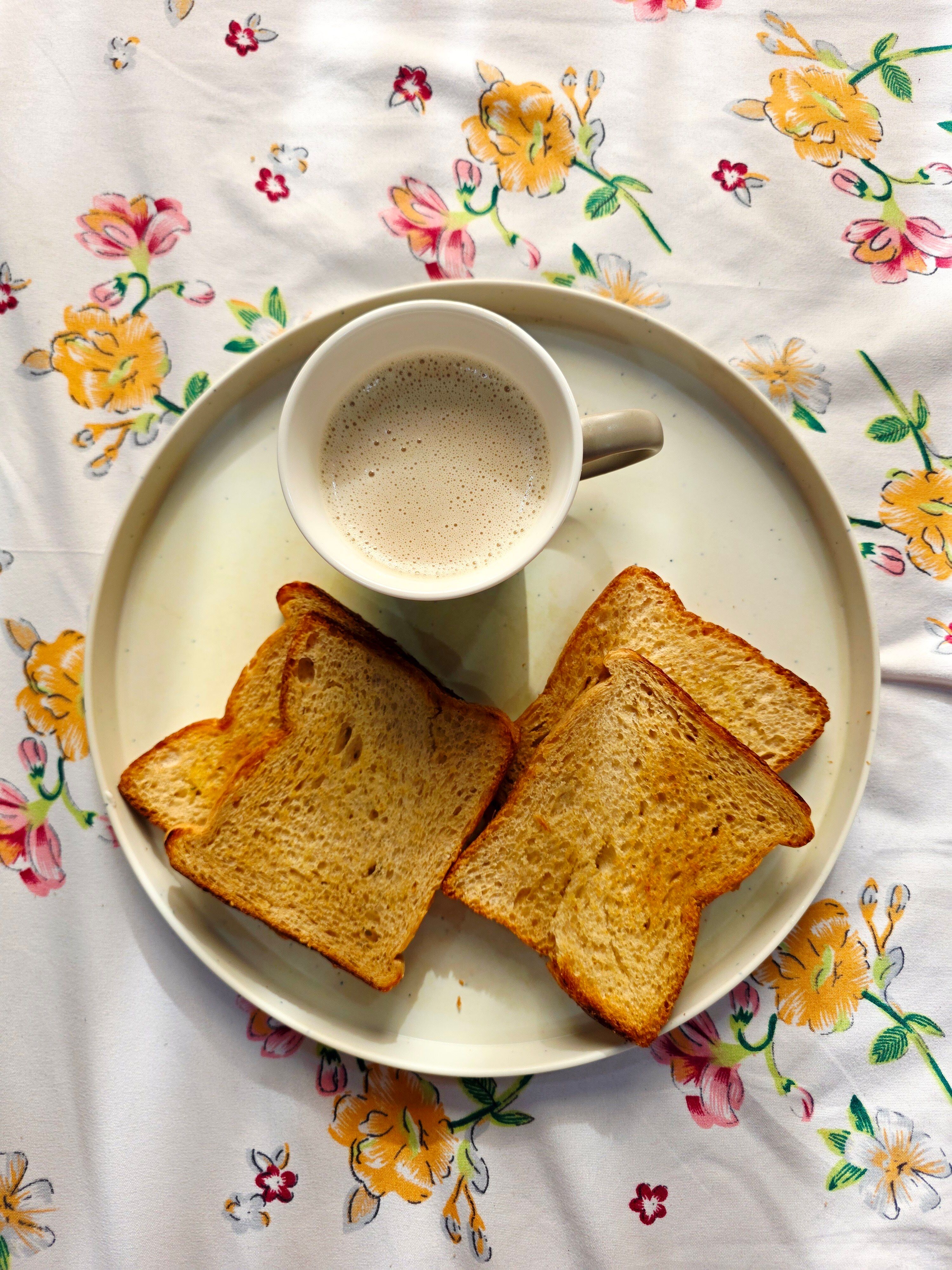 Top view of a breakfast setup with coffee and toasted bread on a floral tablecloth.