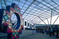Vibrant signage at a bustling indoor expo event with attendees gathering and colorful lighting.