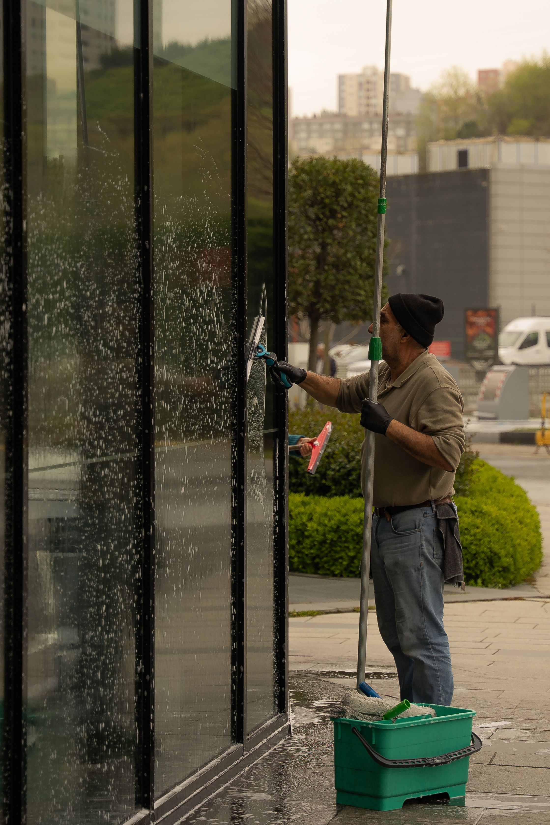 Un laveur de vitres passe la raclette sur la façade en verre d'un immeuble, par temps couvert