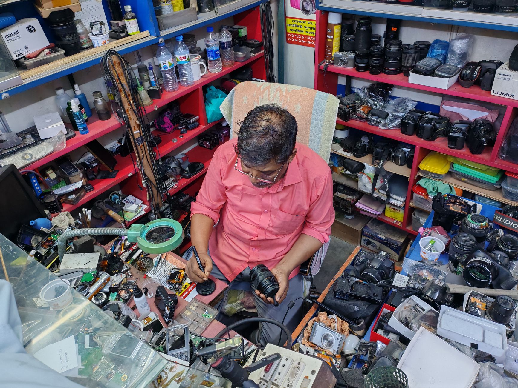 A camera technician in a workshop examining and repairing a camera lens amidst various tools and equipment.
