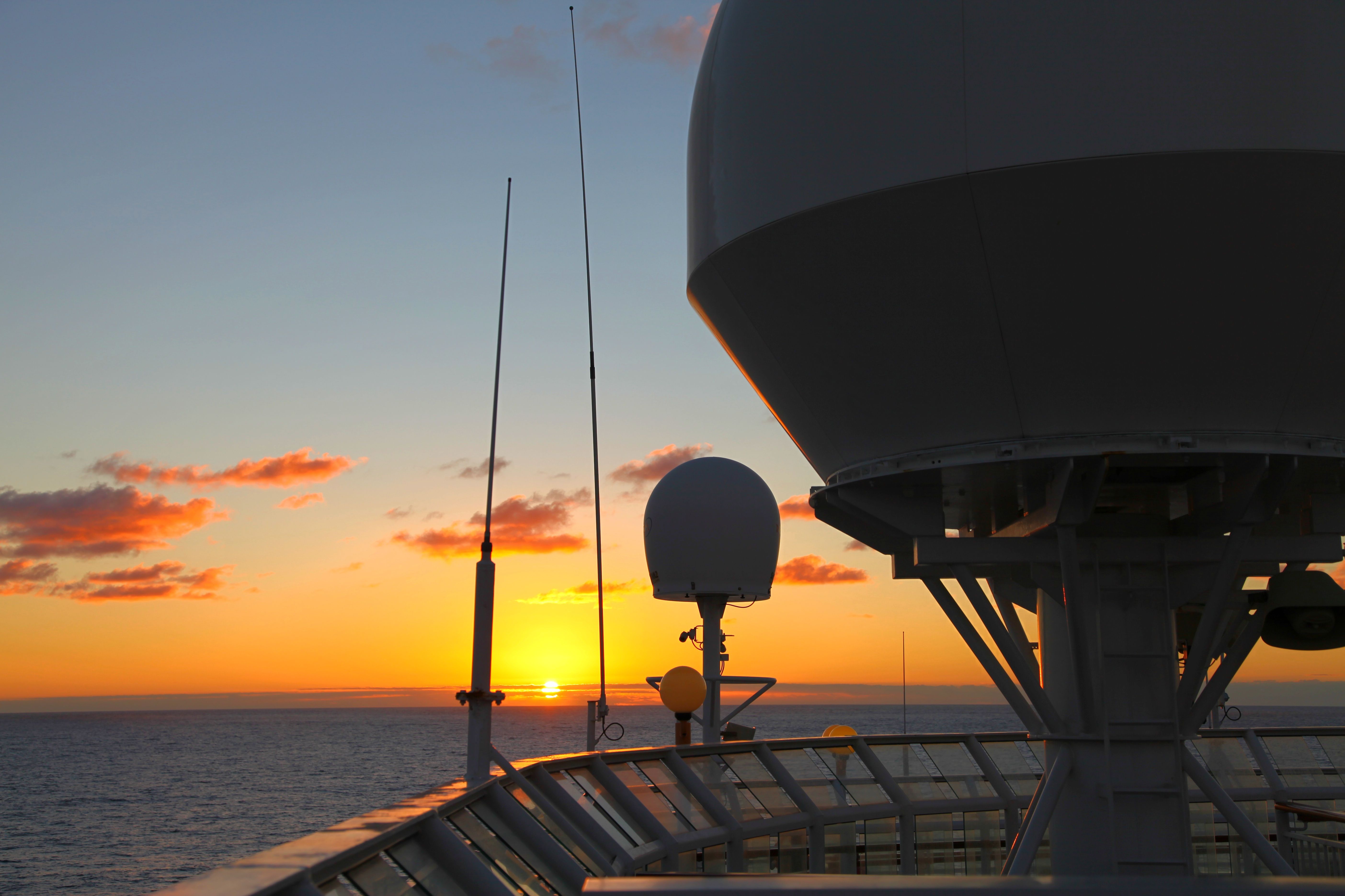 Sunset over ocean with ship radar equipment in the foreground, creating a serene maritime scene.