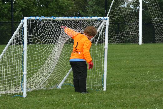 A child goalkeeper in bright uniform gears up on a soccer field.