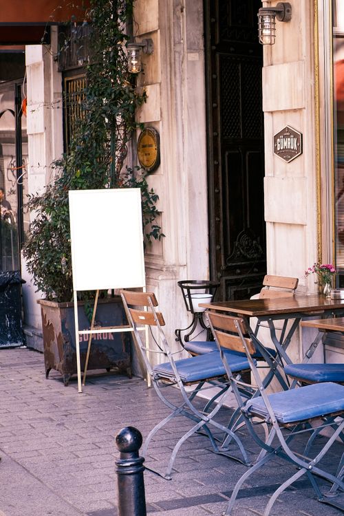 Free Cozy street cafe with wooden chairs, empty sign, and ivy on a sunny day. Stock Photo