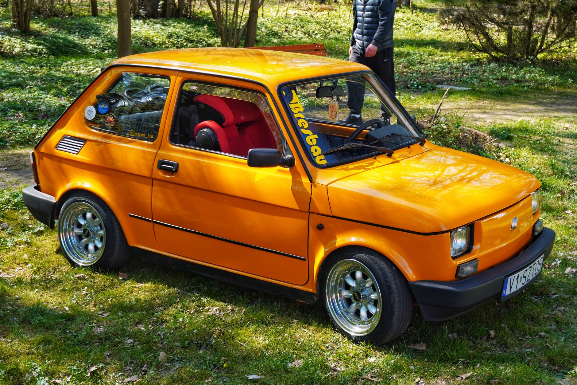 Classic Fiat car in vivid orange parked in a sunny green park.