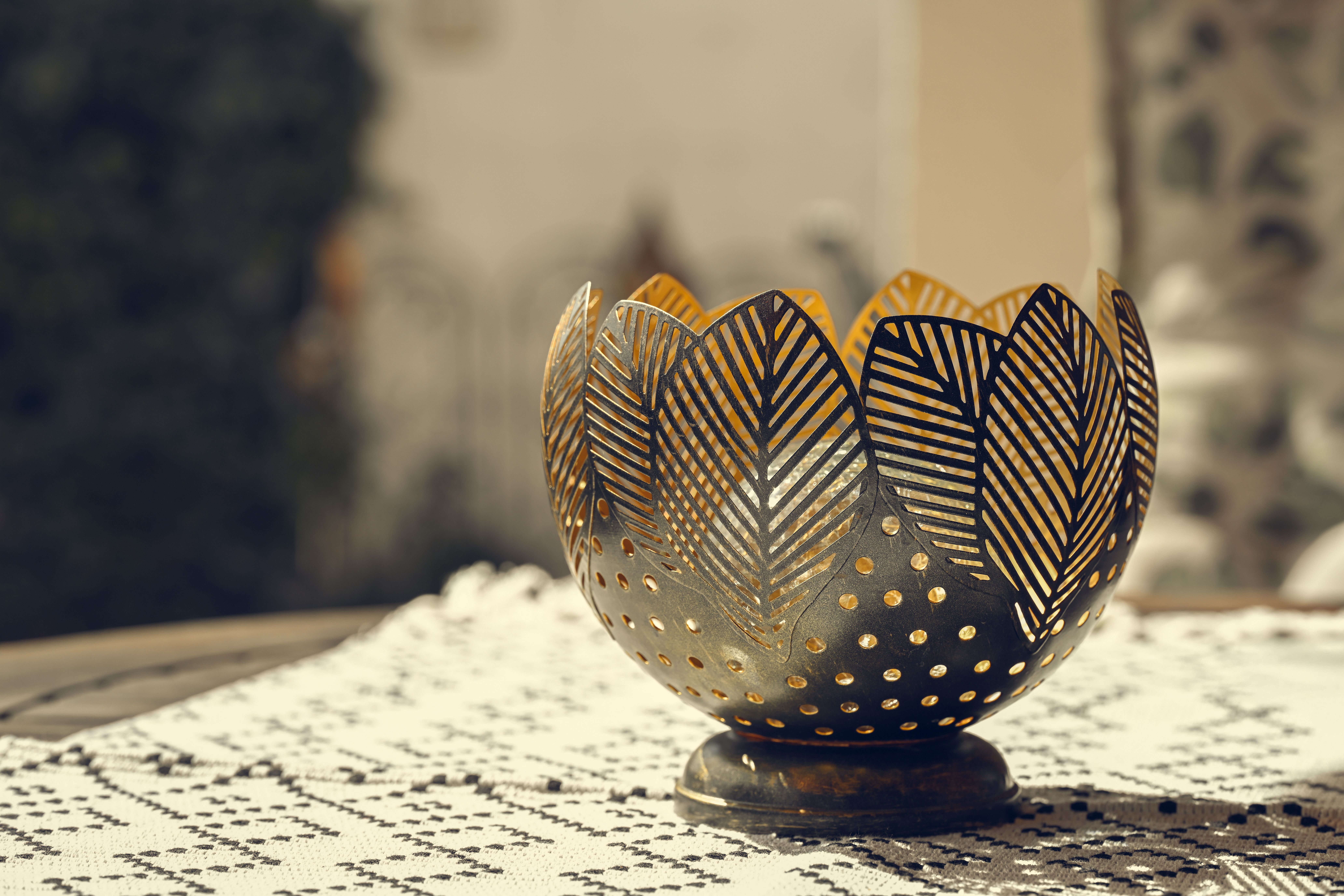 A decorative metal bowl featuring intricate leaf patterns on a lace tablecloth, outdoors in daylight.