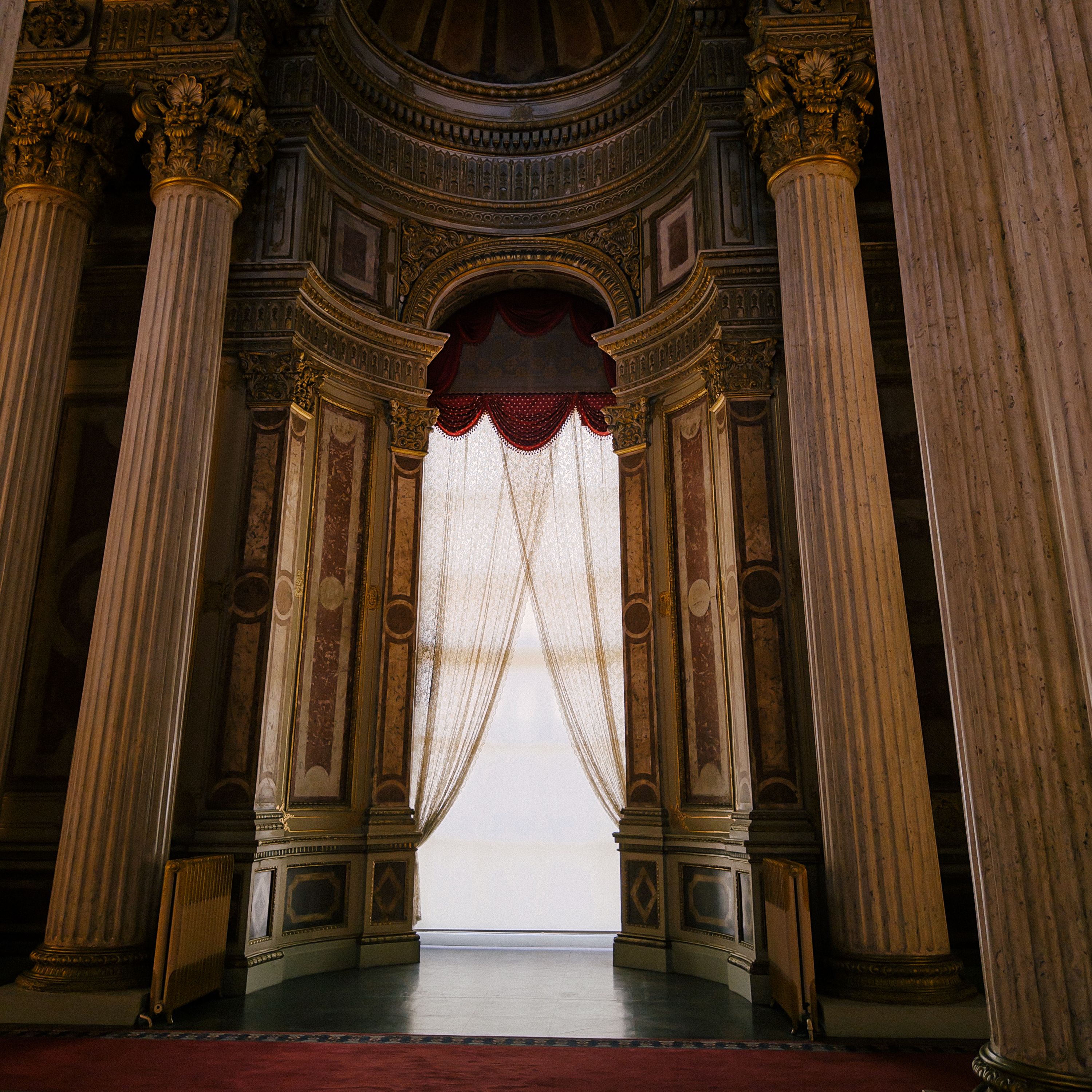Grand architectural interior with arched window and ornate columns, evoking a historical elegance.