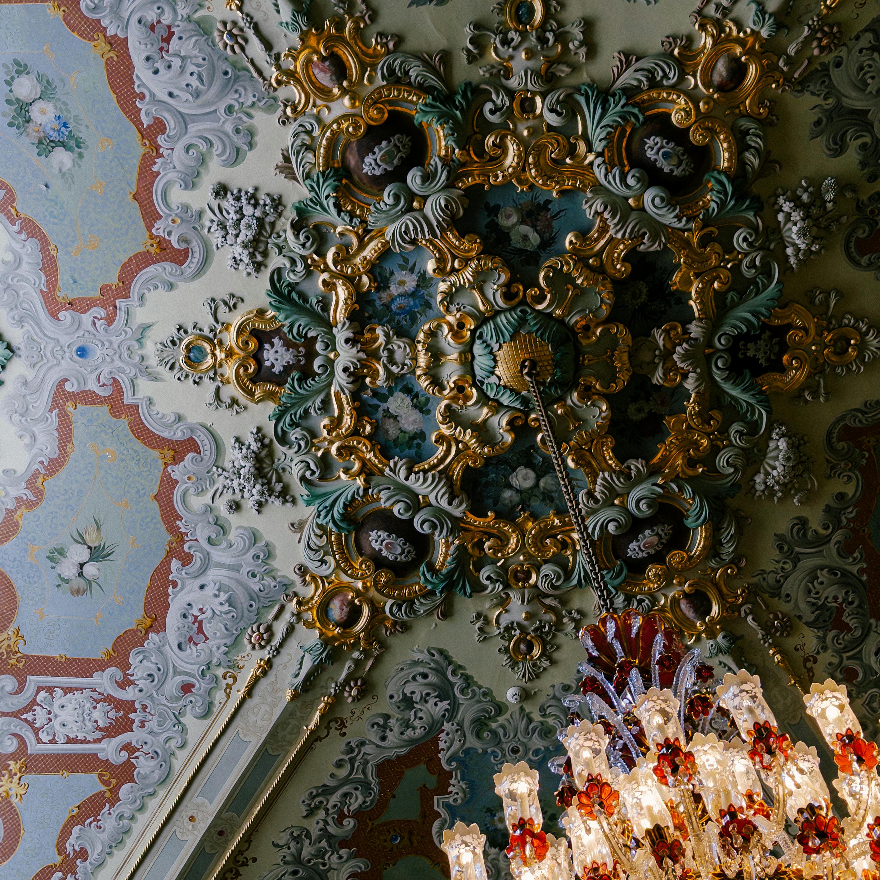 A richly decorated Baroque ceiling with a luxurious crystal chandelier, showcasing intricate gold detailing.