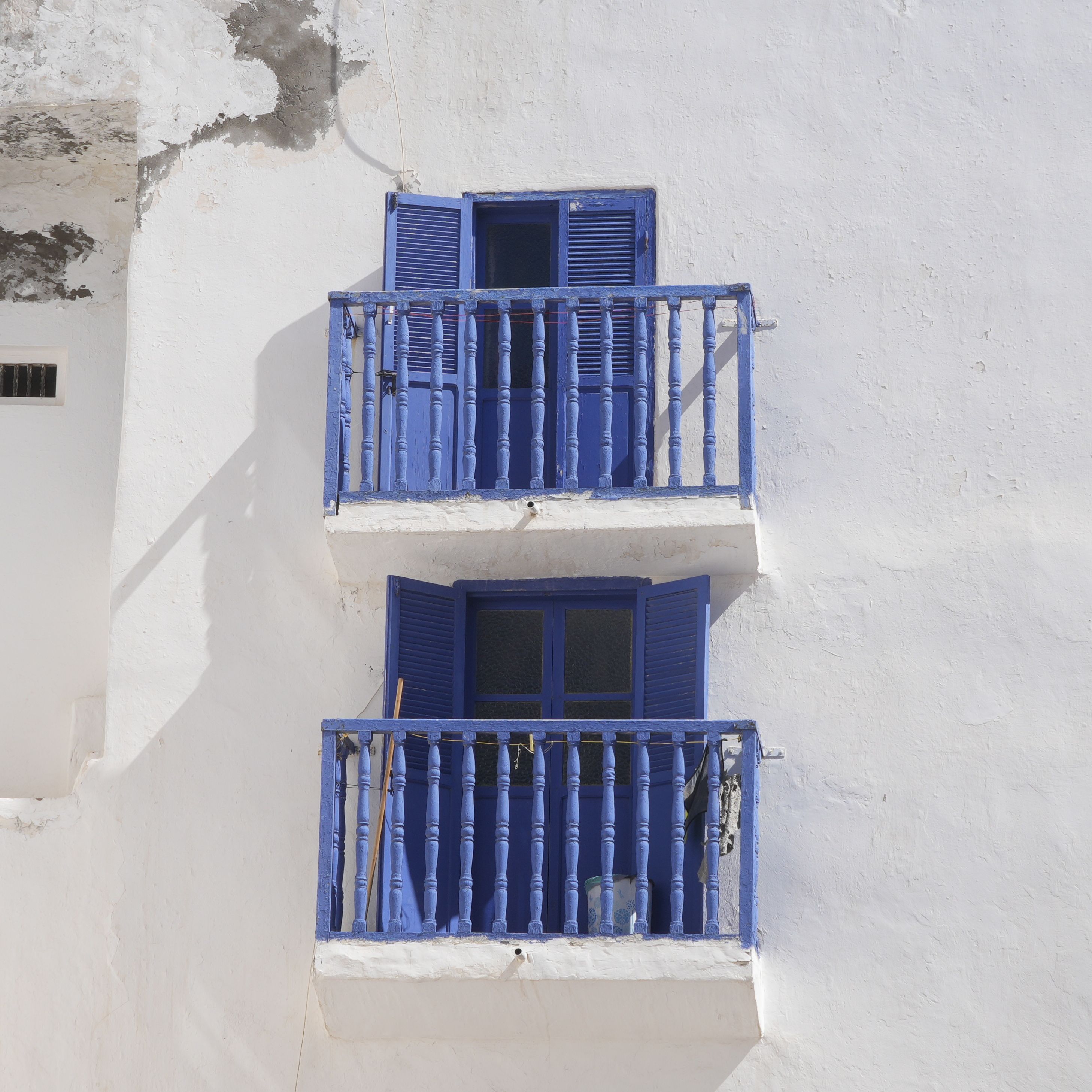 Blue shuttered balcony windows on a whitewashed wall in Essaouira, Morocco, under clear daylight.