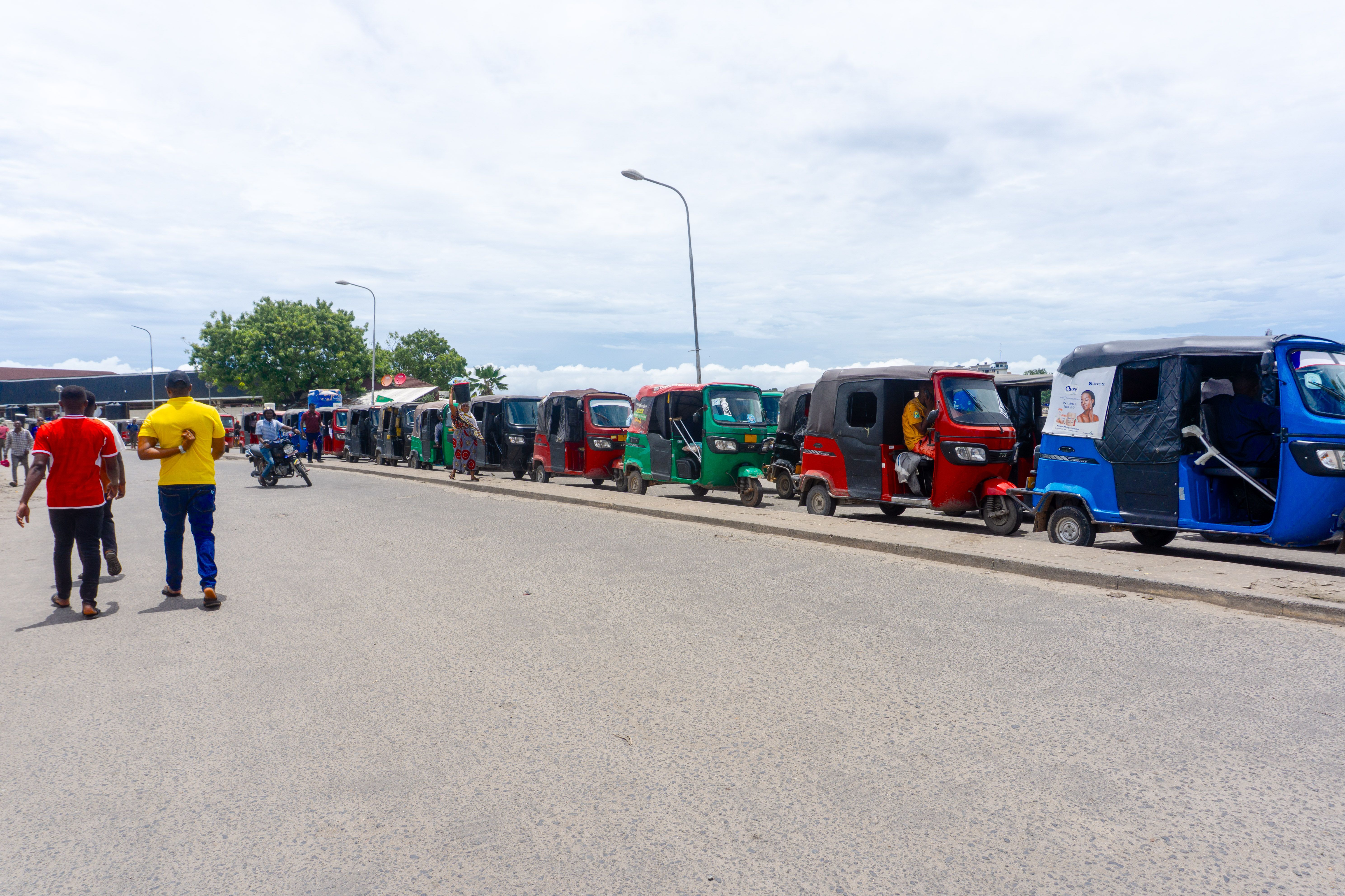 A row of vibrant tuk-tuks parked on a bustling urban street, showcasing everyday commute life.