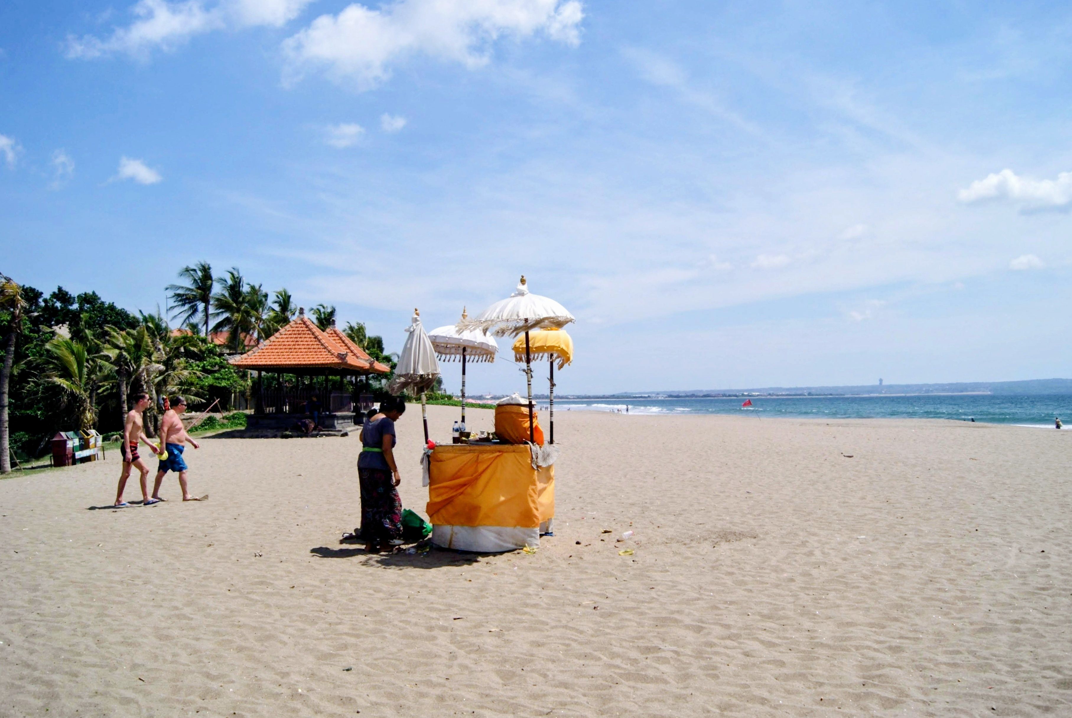 A serene beach scene in Bali featuring traditional Balinese umbrellas and a wide sandy shore.