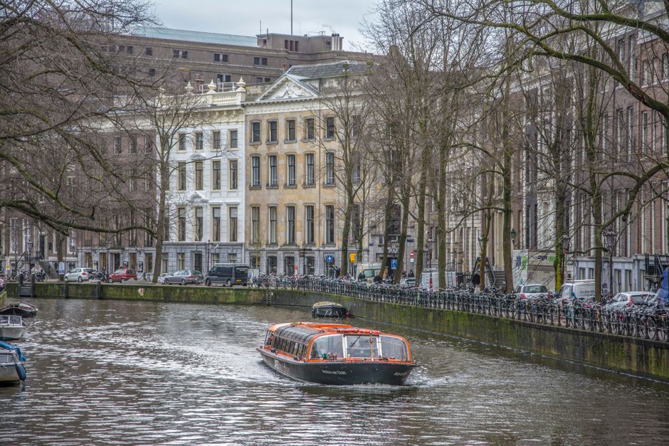 A scenic view of Amsterdam's historic canal with a tour boat surrounded by classic architecture in winter.