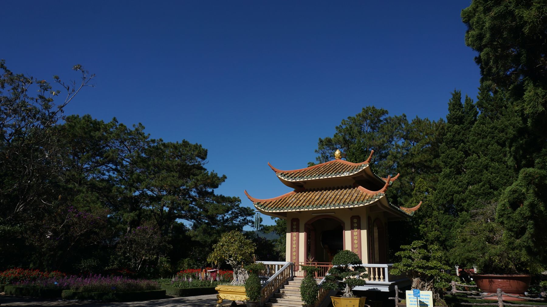 Pagoda tradisional yang dikelilingi oleh tanaman hijau subur pada hari yang cerah di Đà Lạt, Vietnam.