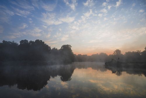 Free A serene view of sunrise over a mist-covered lake with beautiful reflections. Stock Photo