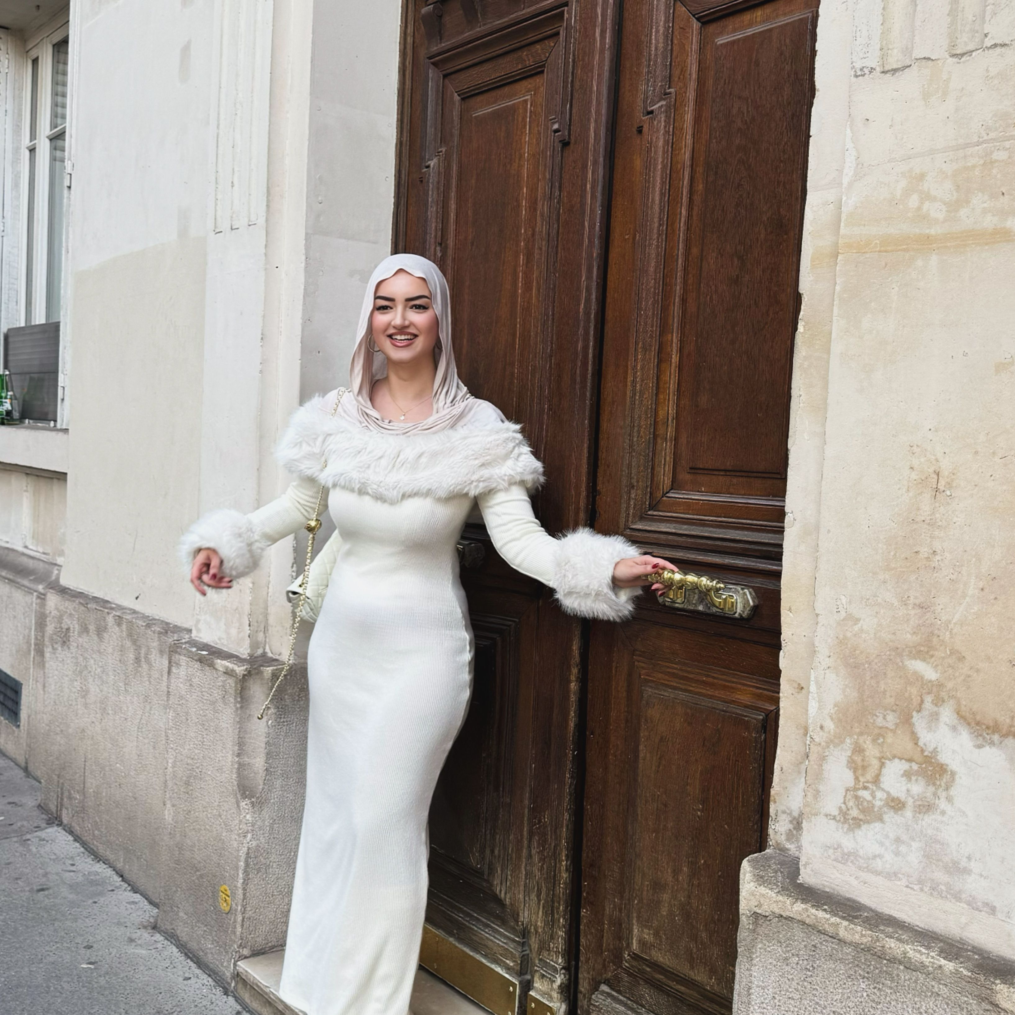 A fashionable woman in a white dress stands outside a classic Parisian building, exuding elegance and style.