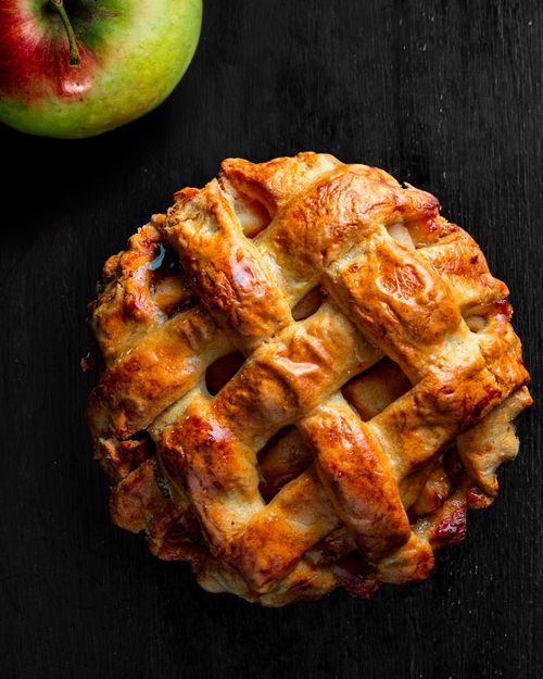 Free Tasty homemade apple pie with lattice crust and a fresh apple on a dark surface. Stock Photo