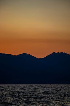A tranquil sunset with a silhouetted mountain range and calm sea, capturing the beauty of nature.
