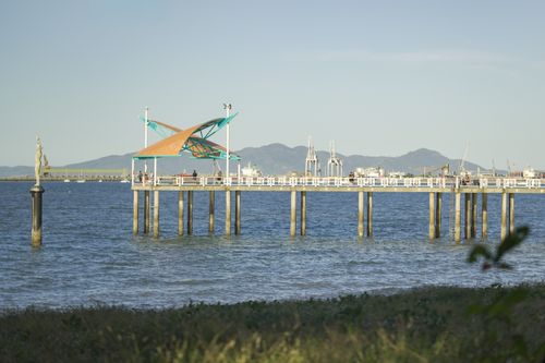 Free A picturesque pier extends into the ocean, topped with a striking angular canopy, against a backdrop of distant mountains at sunset. Stock Photo