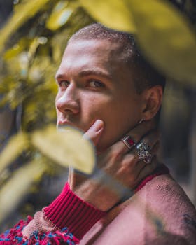一位穿着粉色毛衣、戴着时尚戒指的年轻人，在树叶环绕中拍摄的特写肖像