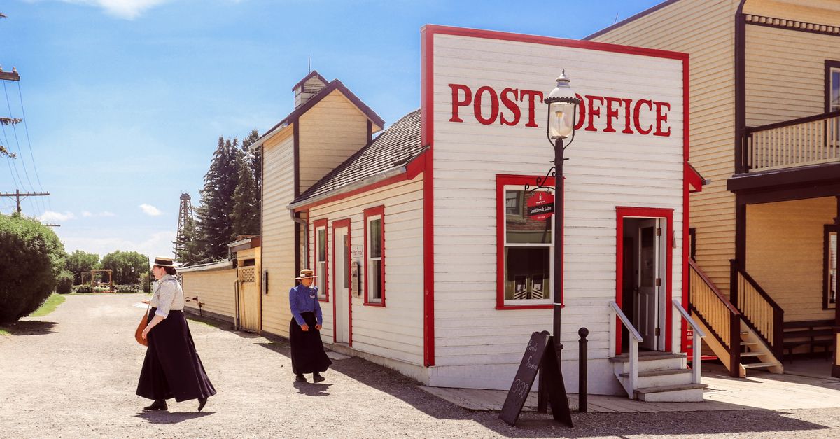 Vintage-style photo of a historic post office at Heritage Park in Calgary with people in period attire.