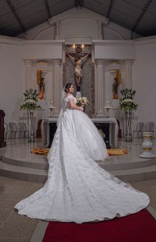 Bride in a church wearing a white gown, holding a bouquet, standing at the altar in Santo Domingo de los Tsáchilas, Ecuador.