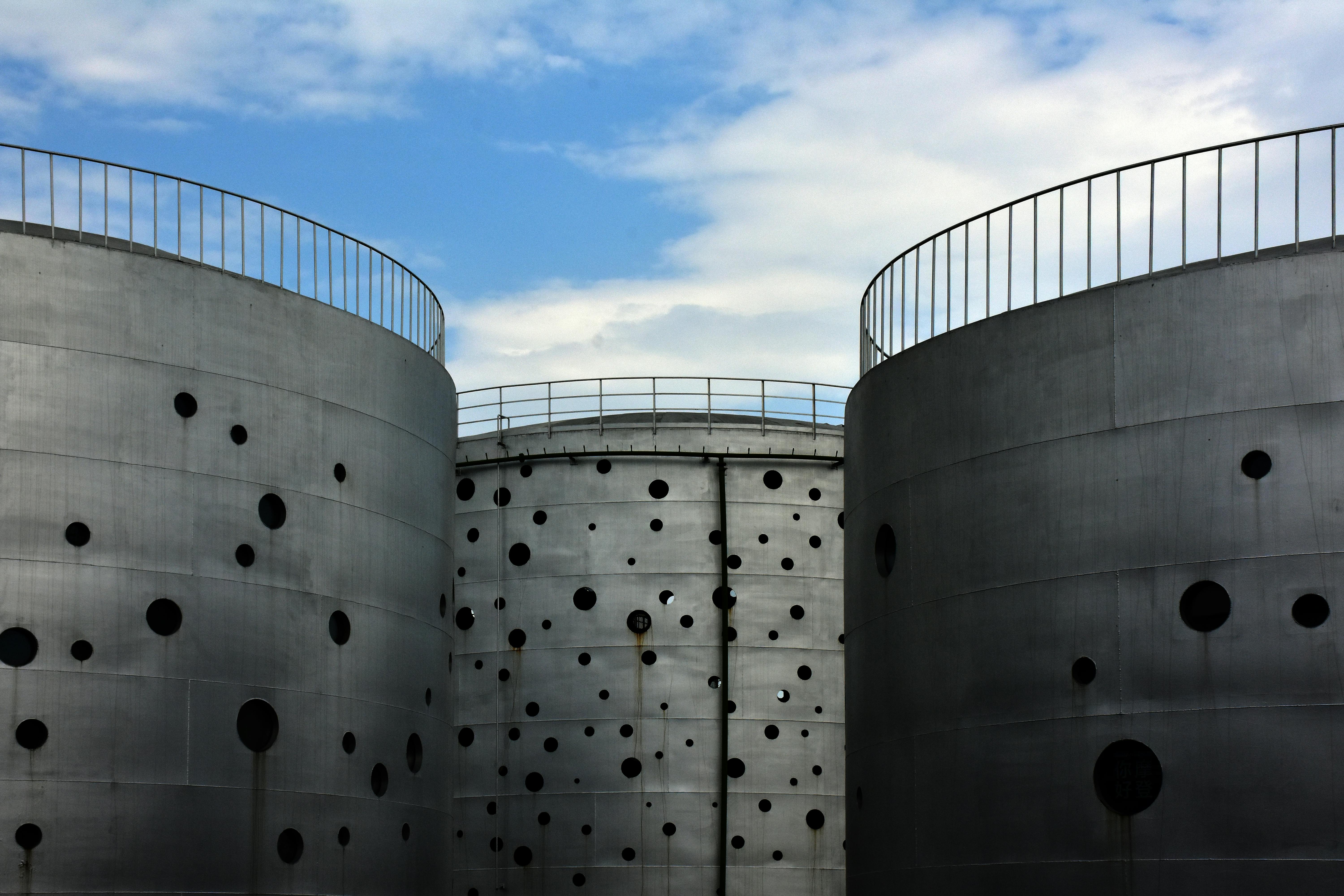 Large metal silos with perforated design standing under a clear blue sky in an industrial setting.