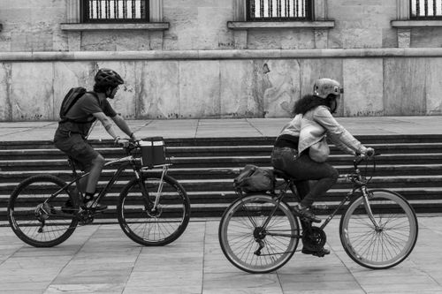 Free Black and white photo of two cyclists with helmets riding past urban street steps. Stock Photo