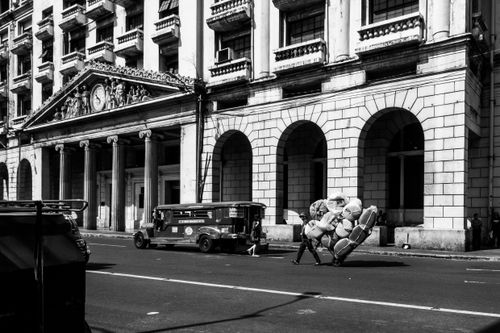 Free A monochromatic city street scene featuring a historic building with arches and a jeepney passing by. Stock Photo